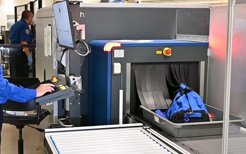 An operator loading baggage into a CT scanner on an airport terminal screening lane