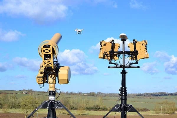 Two mast-mounted anti-drone detection and jamming systems tracking a small UAV over open country